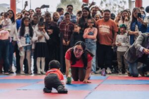 Un bebé gatea hacia una mujer arrodillada con un juguete, ante el público, en el Concurso de Gateo de Tlaxcala