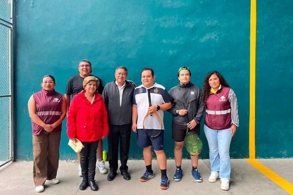 Siete personas posan junto a un muro de cancha en el Polideportivo Adolfo López Mateos; dos sostienen raquetas de tenis
