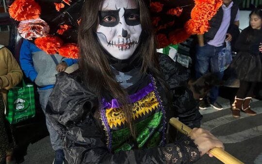 Participante caracterizada como Catrina, con maquillaje de calavera, sombrero con flores naranjas y vestido de papel...