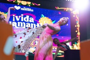 Bailarina con vestido rosa y chal floral baila en el escenario del festival Vida Huamantla 2026, frente a una pantalla...